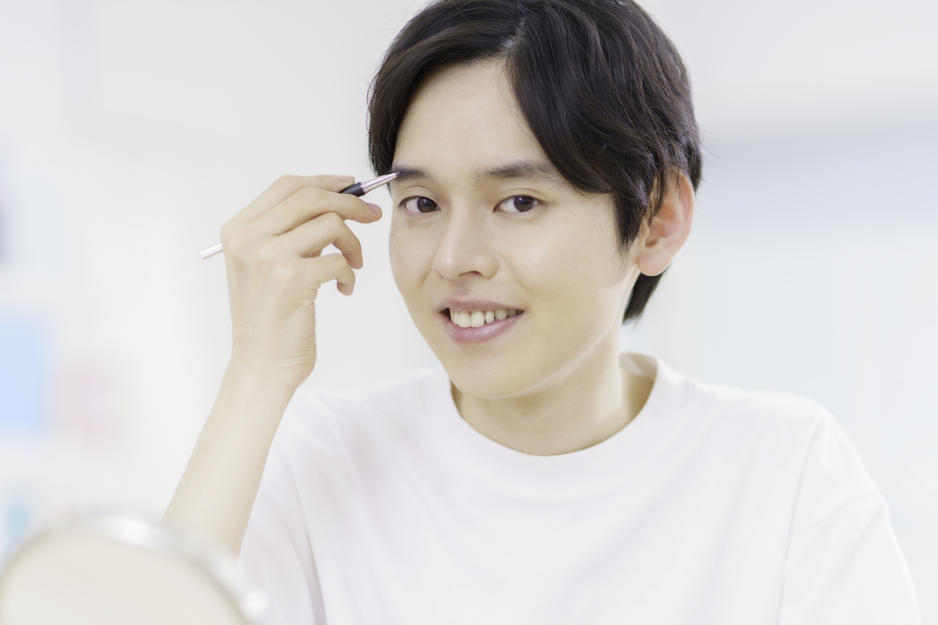 手鏡を見ながら眉毛を整える男性