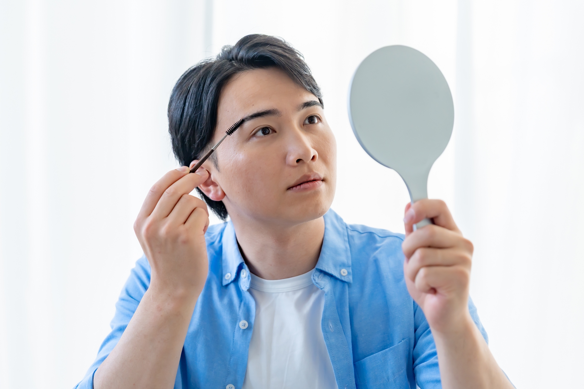 手鏡を見ながら眉毛を描く男性