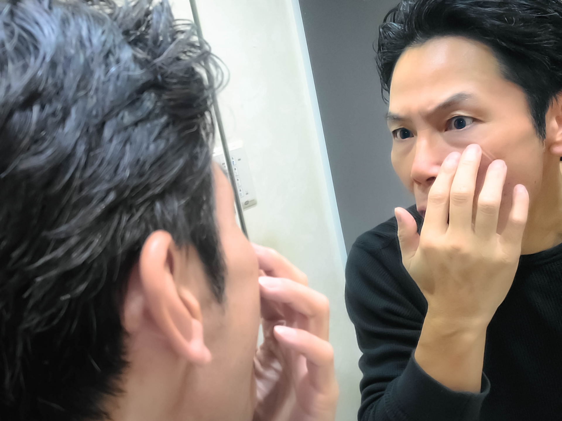 鏡に顔を近づけて眉まわりを確認する男性